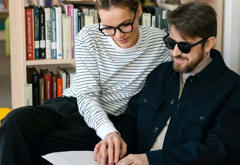 A man reads a braille book with the help of a woman